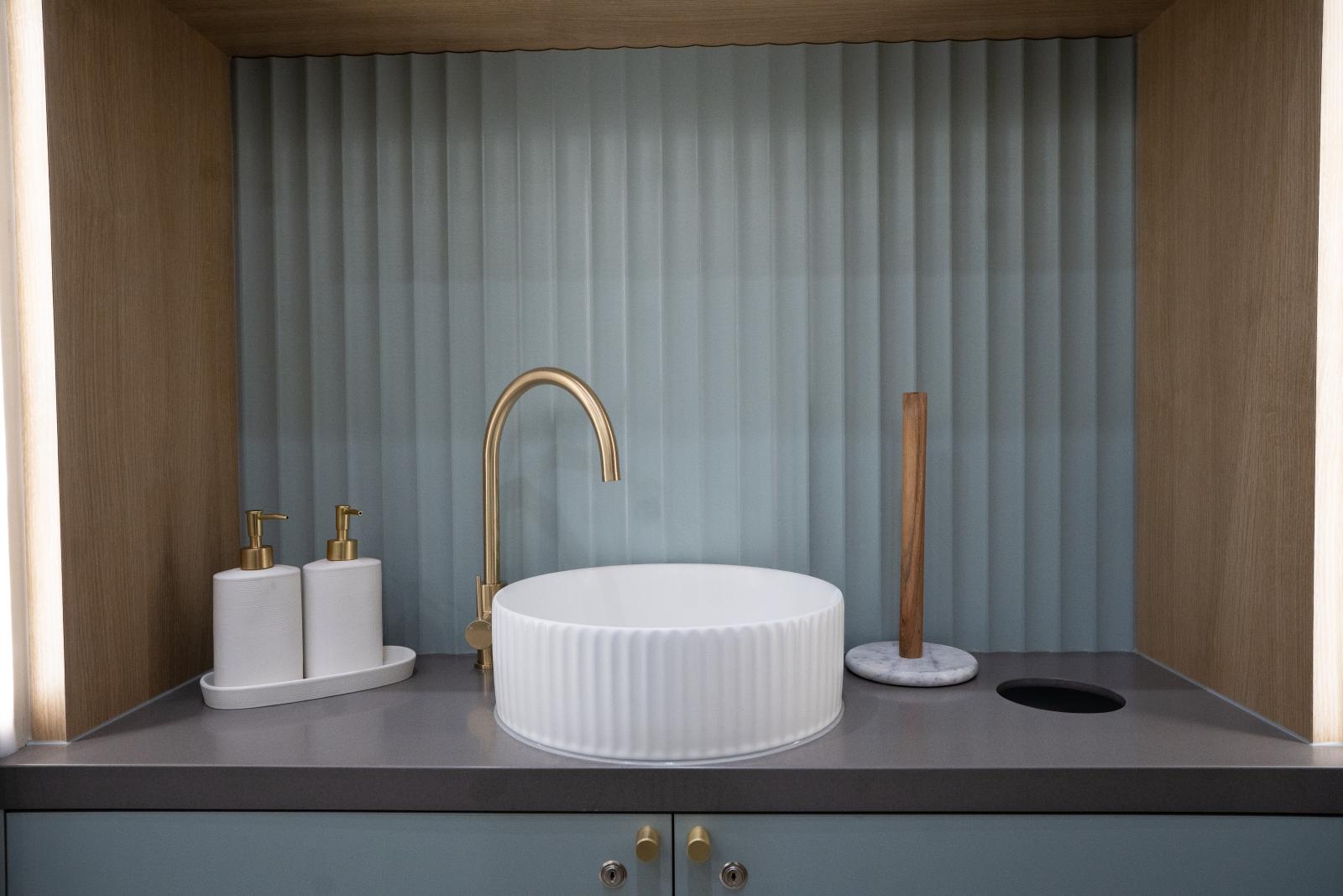 Modern bathroom vanity display with circular white basin, brass tap, and minimalist accessories on grey countertop