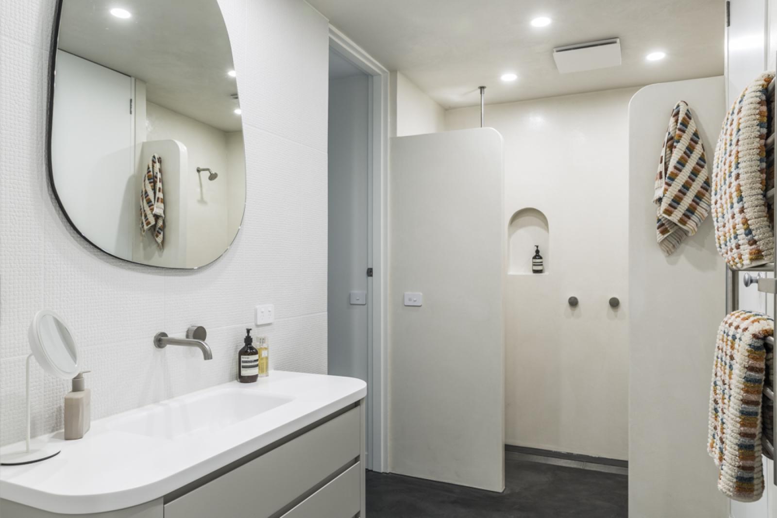 Modern bathroom with white cabinetry, curved mirror, wall-mounted tapware, and walk-in shower with frameless glass doors