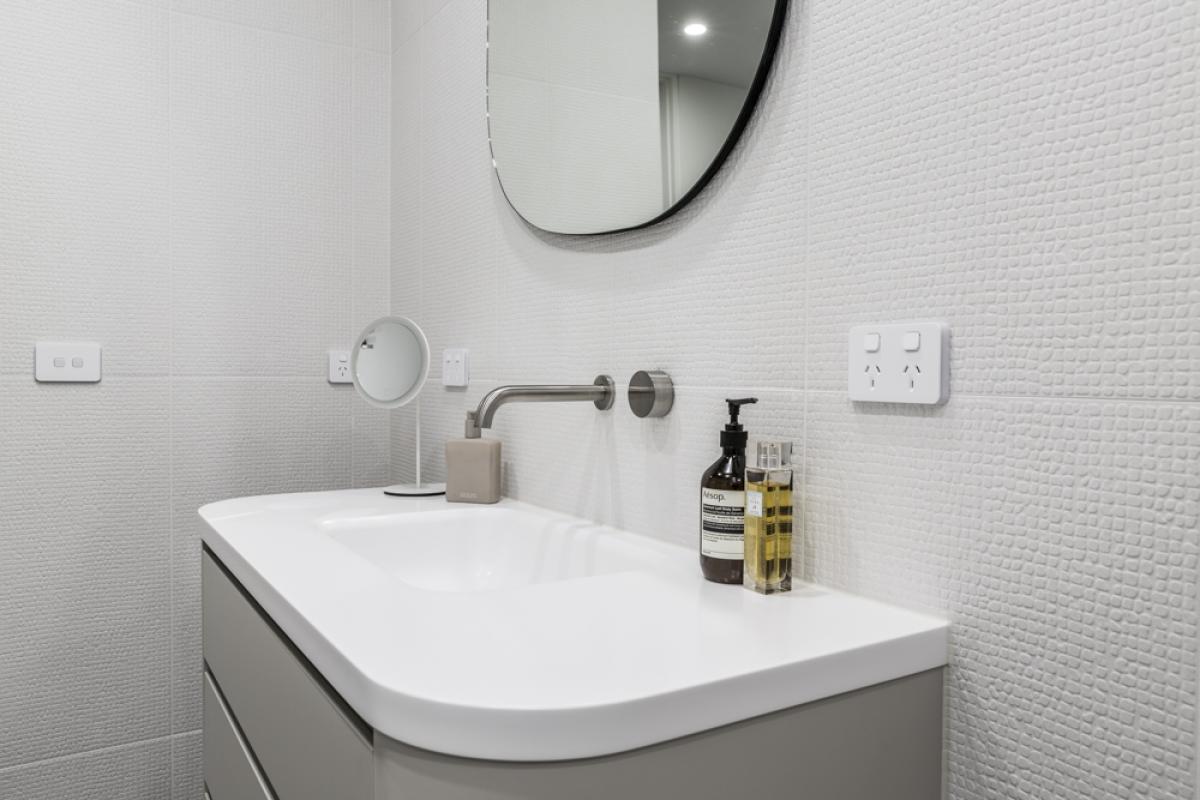 Modern bathroom vanity with white subway tile walls, chrome tapware, and round black mirror