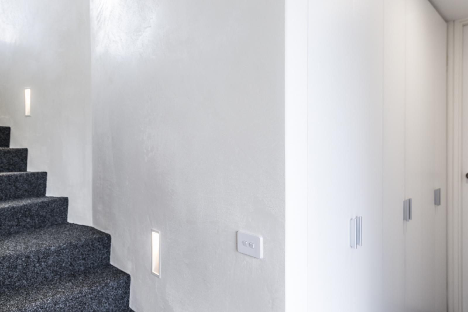 Modern staircase with dark grey carpet runner and white walls featuring contemporary lighting