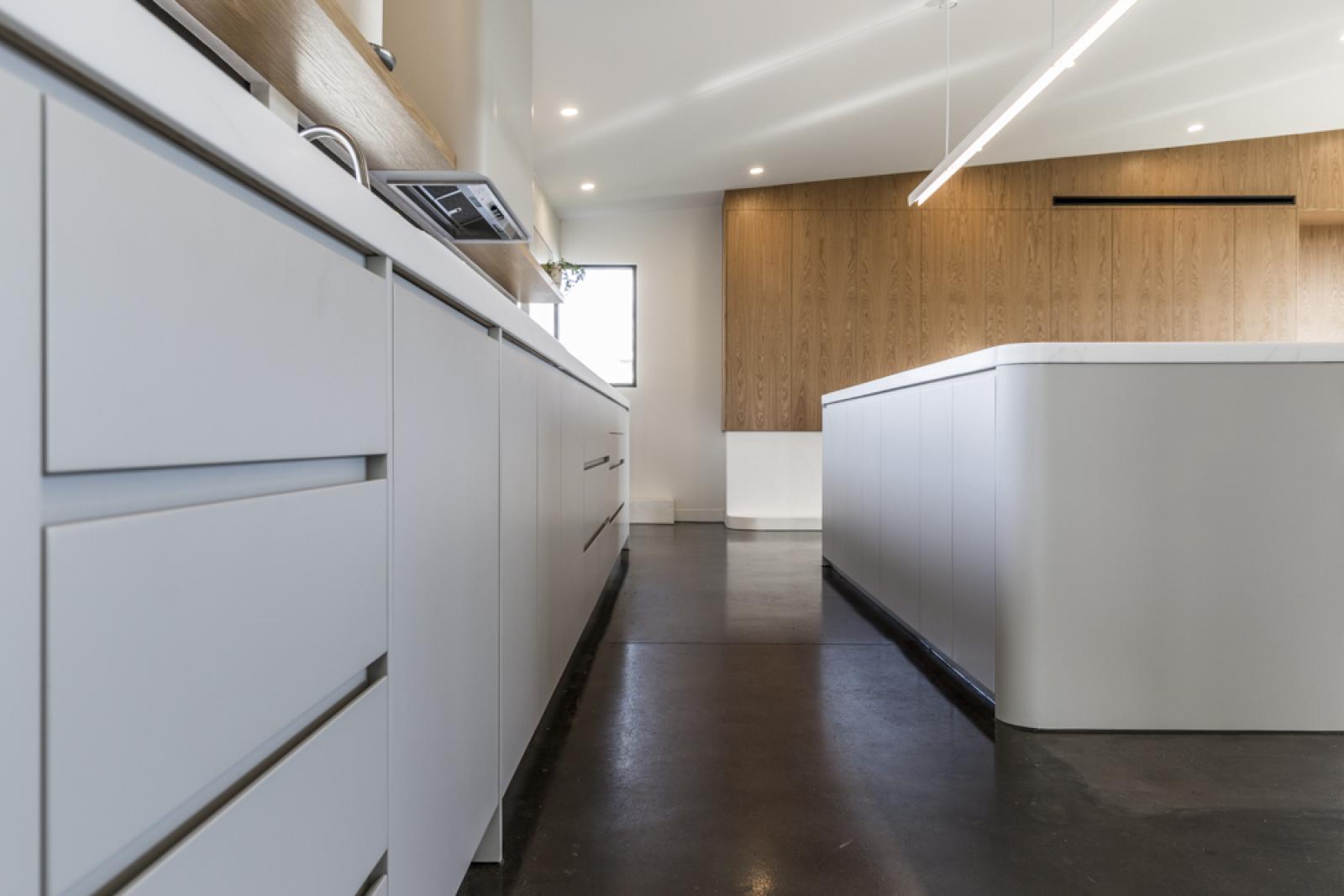 Modern kitchen with white cabinetry, wooden feature wall, polished dark flooring, and recessed lighting
