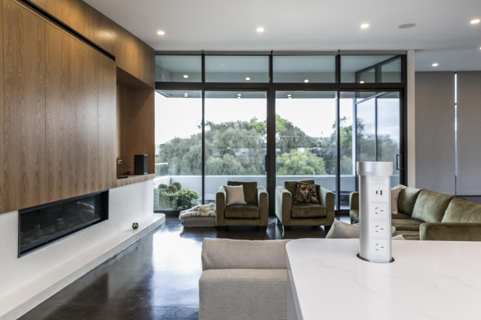 Contemporary open-plan living room with wood feature wall, fireplace, and floor-to-ceiling windows overlooking landscape