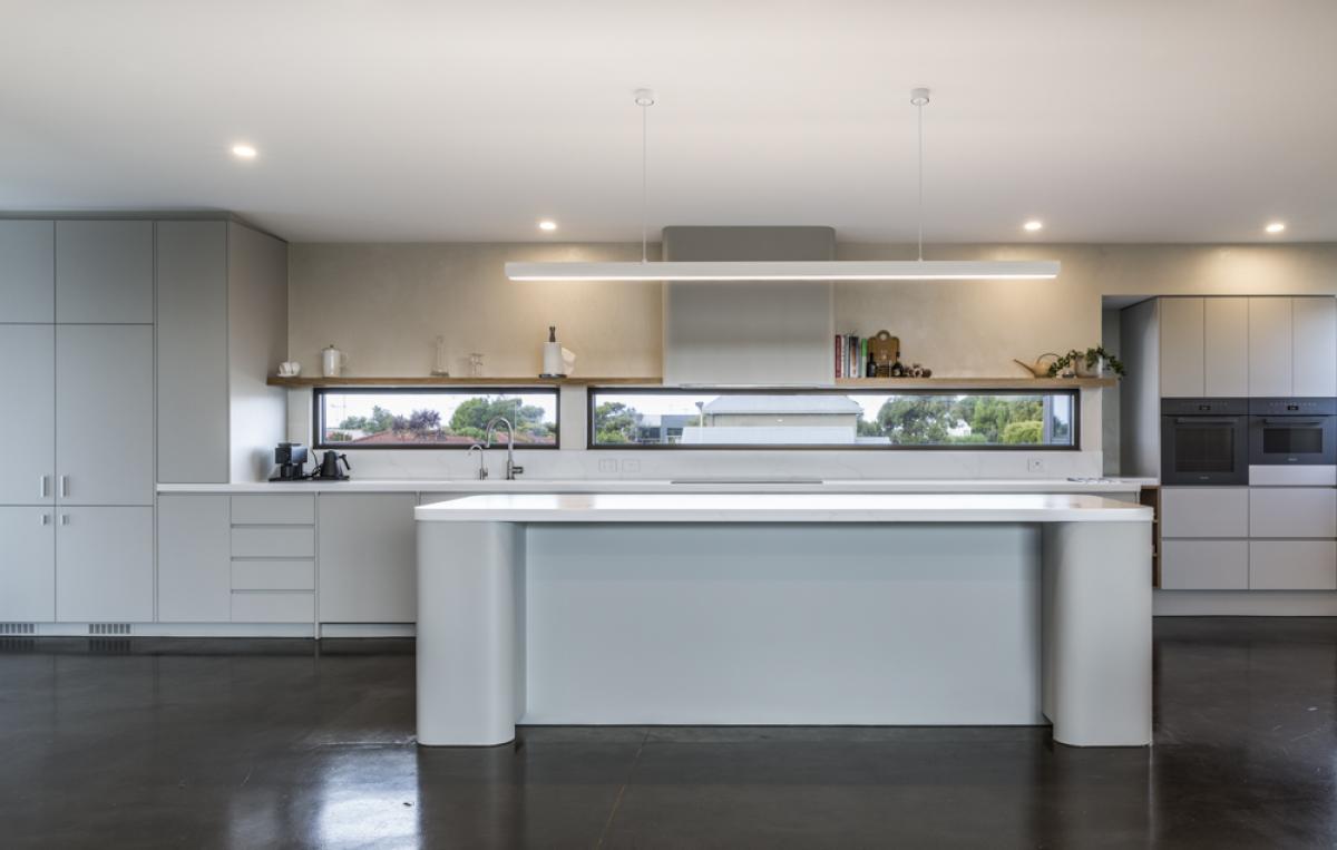 Modern kitchen with grey cabinetry, white waterfall island, and polished concrete flooring