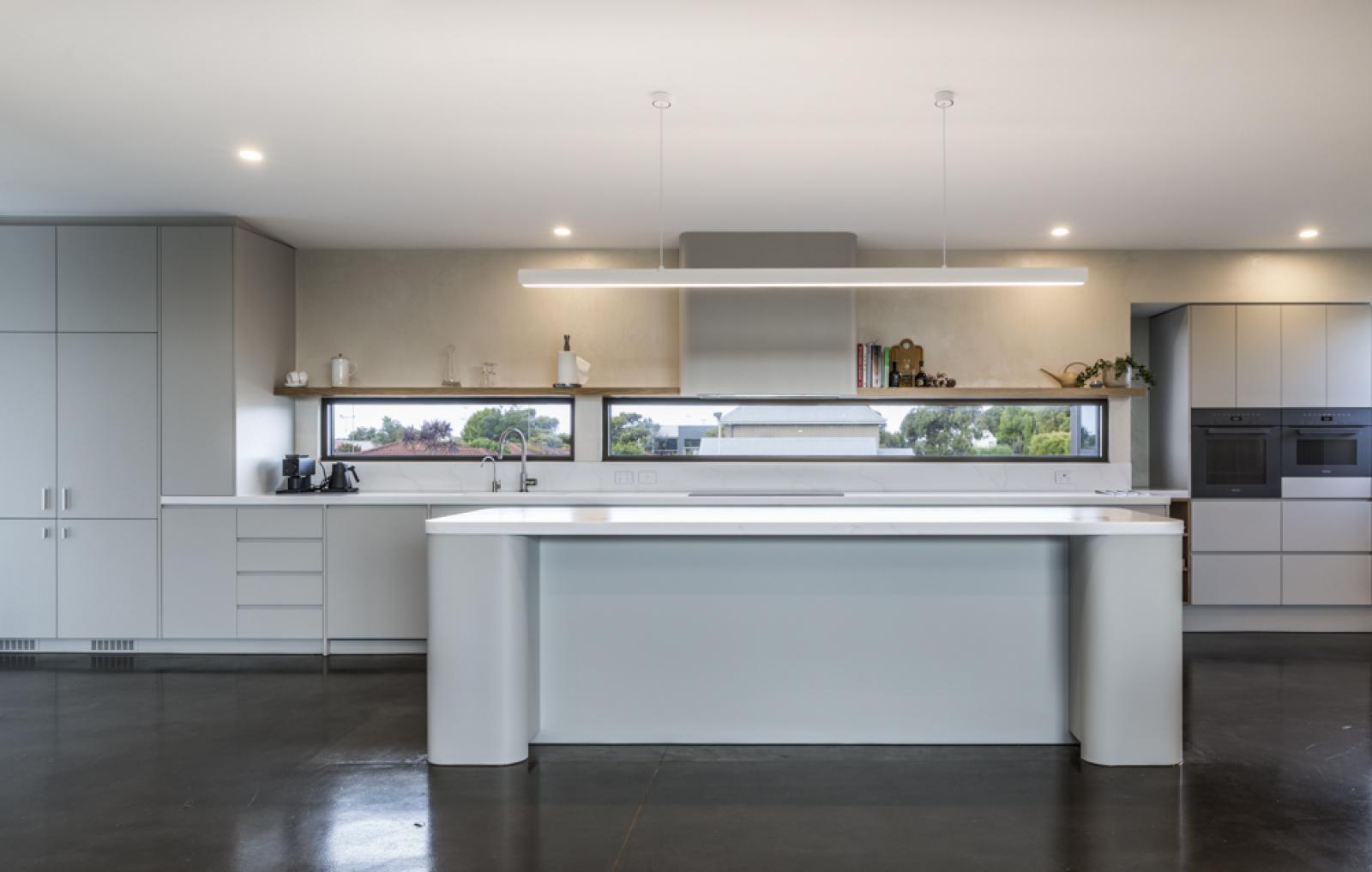 Modern kitchen with grey cabinetry, white waterfall island, and polished concrete flooring