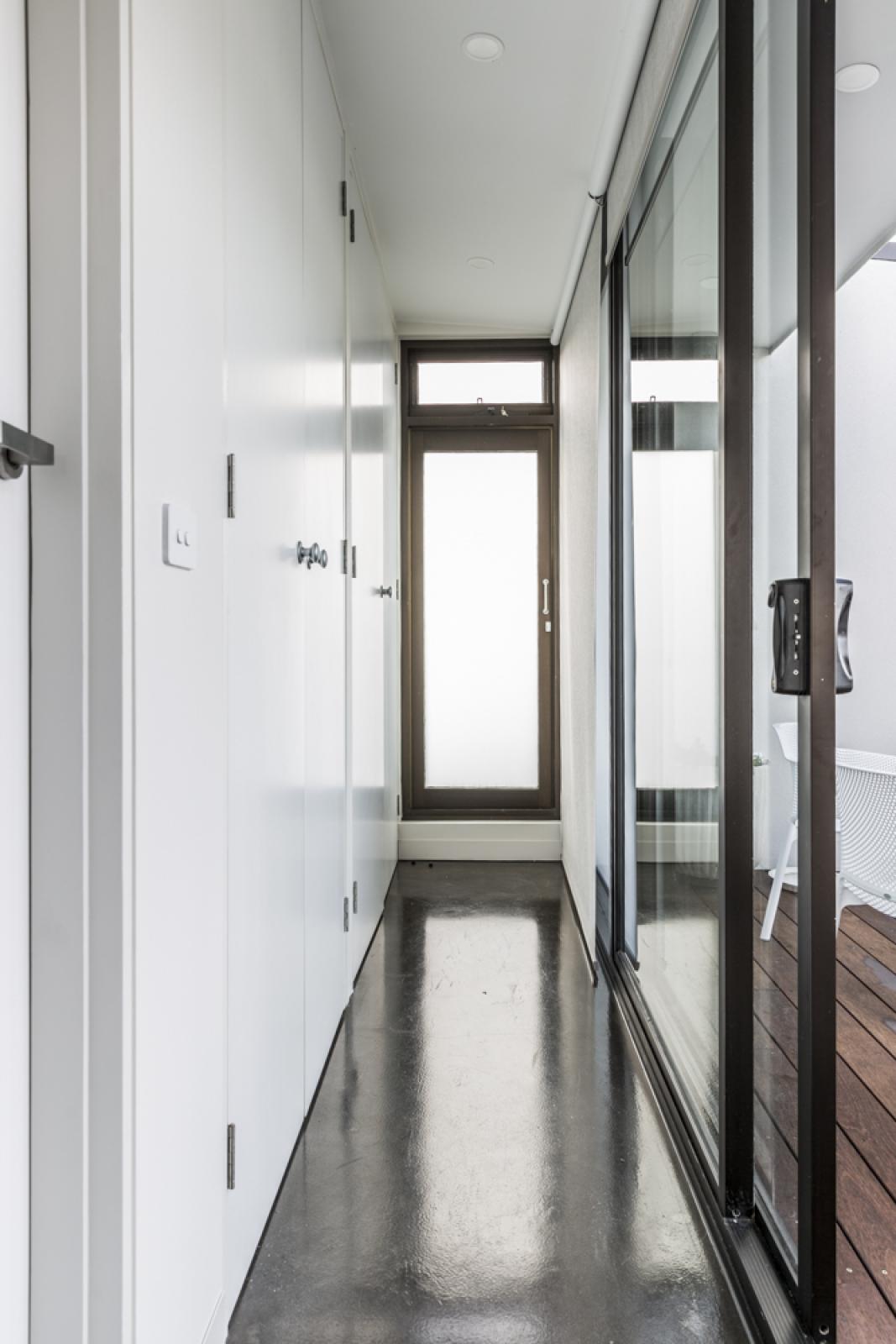Modern hallway with polished concrete flooring, white cabinetry, and frameless glass doors