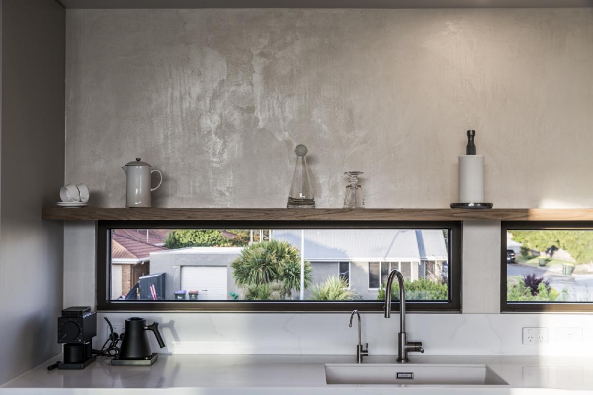 Modern kitchen with white benchtop, black tapware, and polished concrete wall behind sink