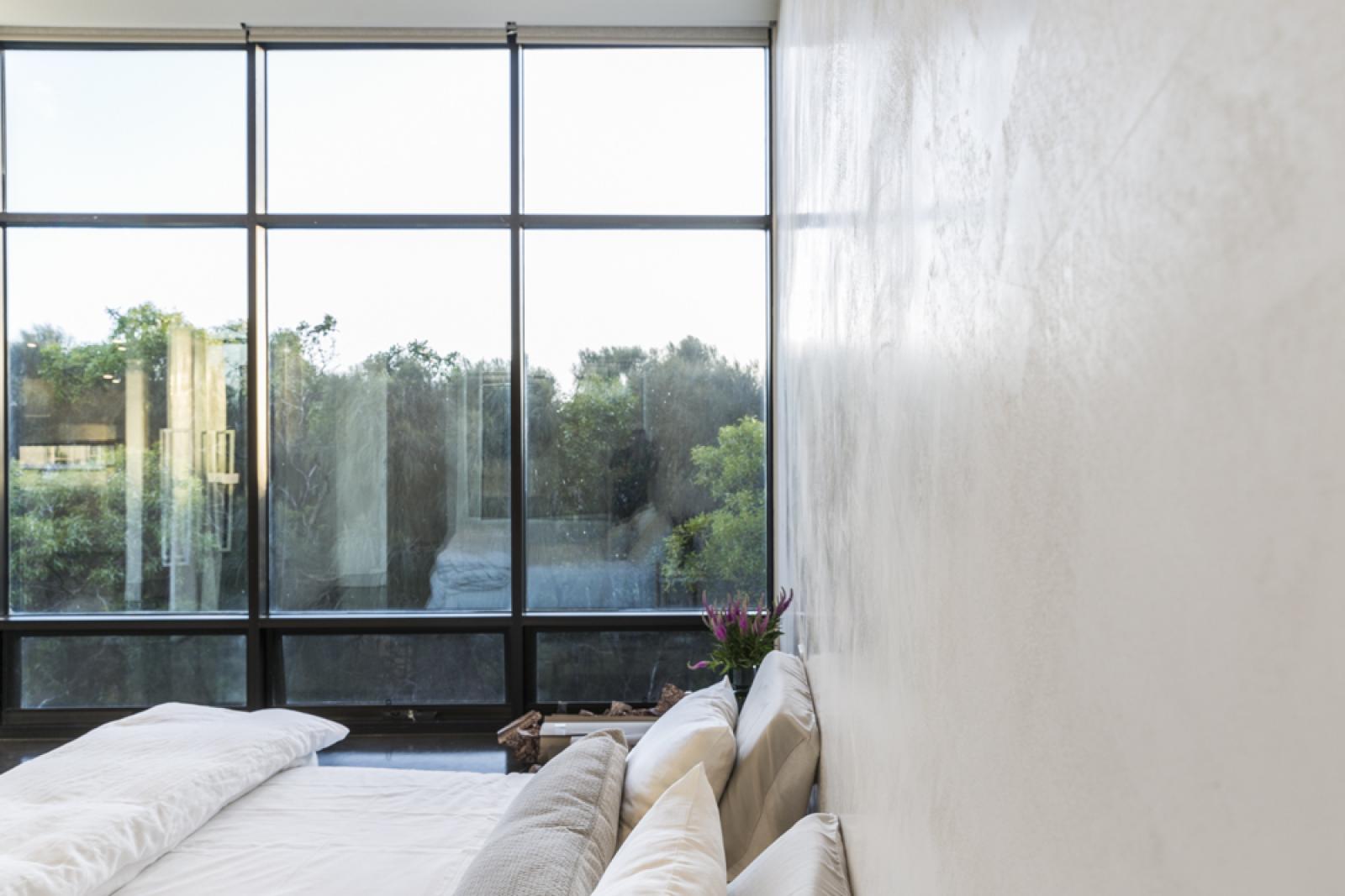 Contemporary bedroom with large black-framed windows overlooking garden views and white bedding