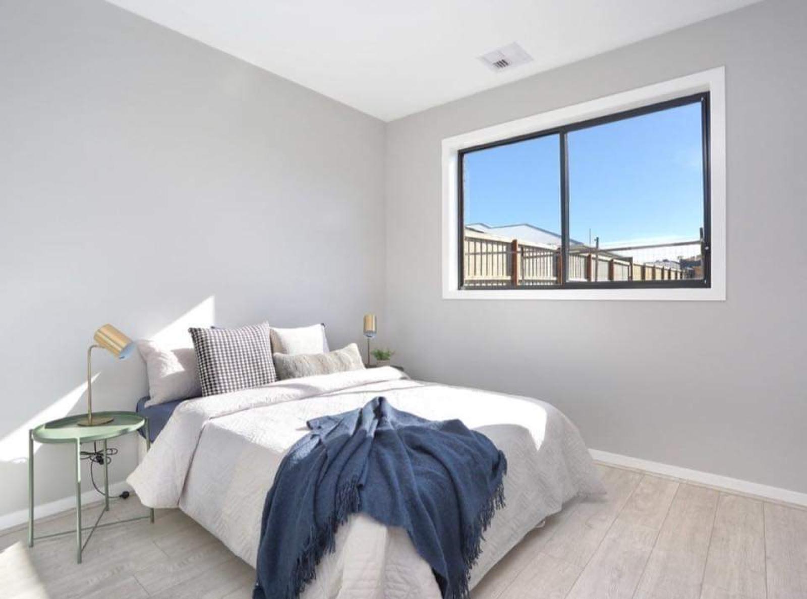 Minimalist bedroom with white bedding, grey walls, and large window overlooking deck