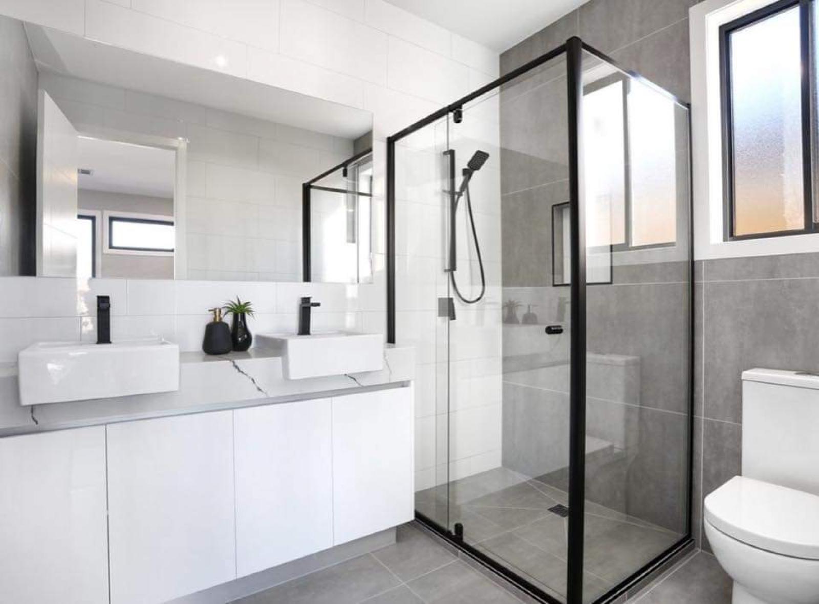 Contemporary bathroom renovation with white cabinetry, dual vanities, black framed glass shower enclosure and grey tile flooring