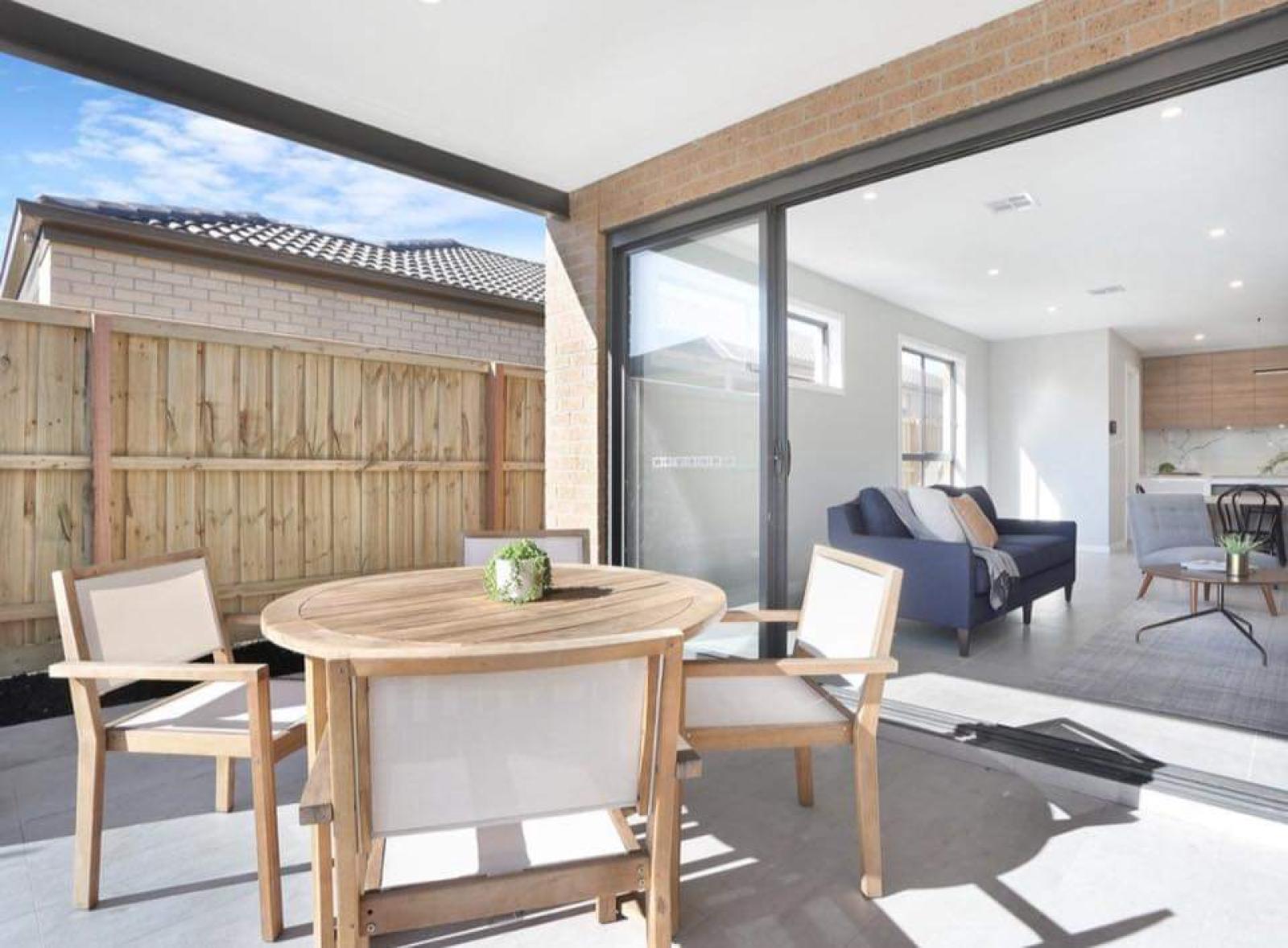 Contemporary outdoor dining area with timber table, chairs, and large glass sliding doors opening to modern interior