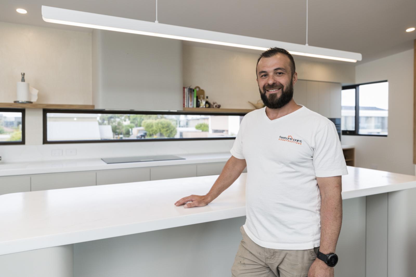 FP Con contractor smiling in modern white kitchen with waterfall island and pendant lighting